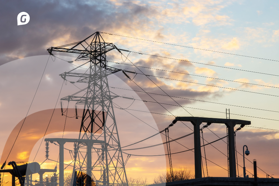 Infraestructura eléctrica de alta tensión con torre de transmisión y líneas eléctricas al atardecer.